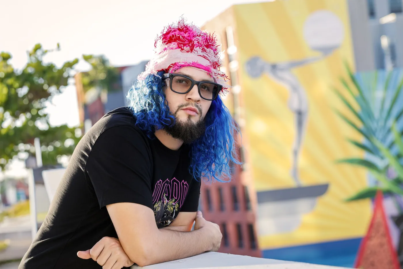 Fly South outdoors in a pink hat and black tee in front of a colorful painted wall