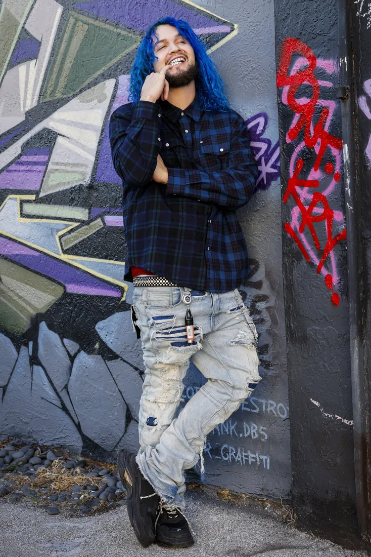 Fly South smiling beside a graffiti wall