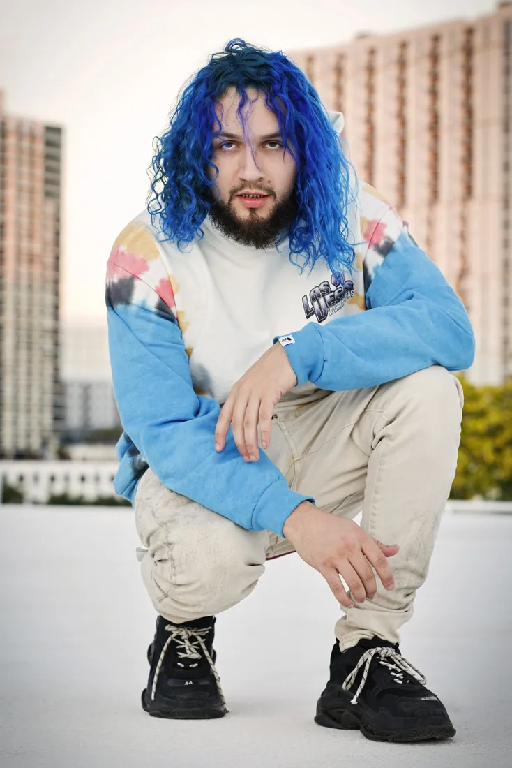 Fly South crouching outdoors in a white and blue hoodie, a different pose