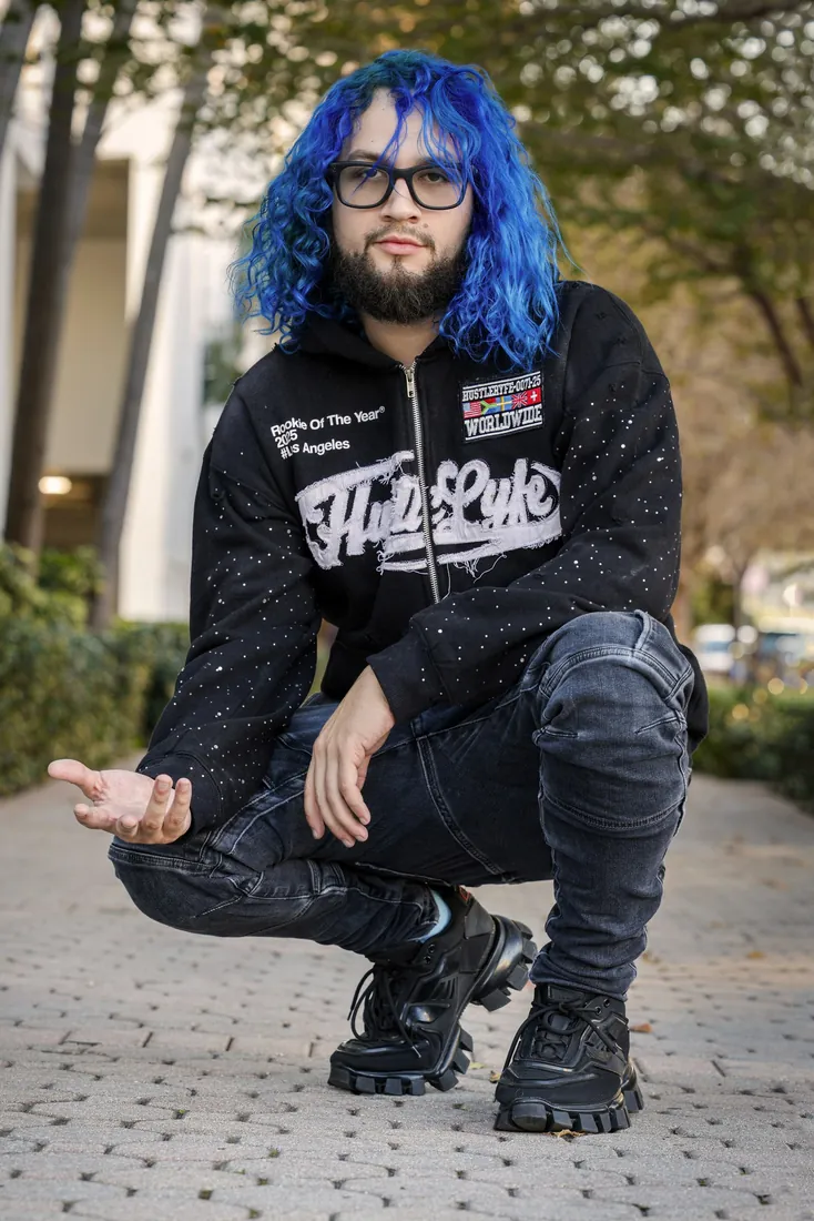 Fly South crouching outdoors in a black hoodie