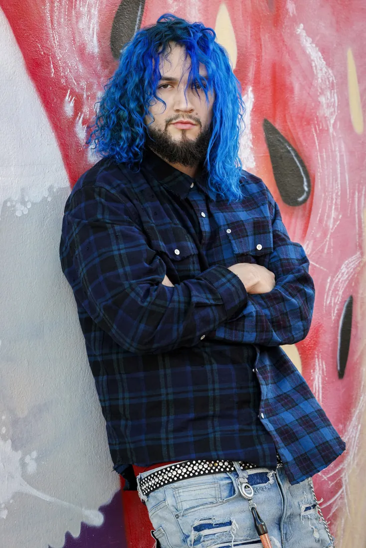 Fly South in a blue plaid shirt with arms crossed in front of a red graffiti wall